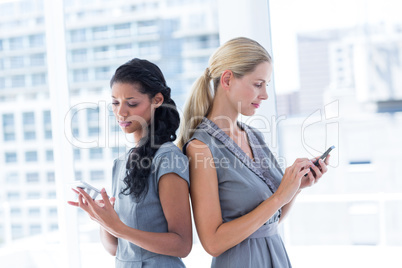 Back to back businesswomen texting messages