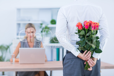 Businessman hiding flowers behind back for colleague