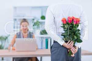 Businessman hiding flowers behind back for colleague