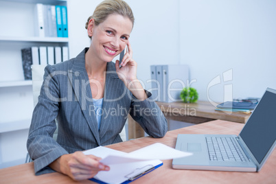 Pretty blonde businesswoman phoning and using her laptop