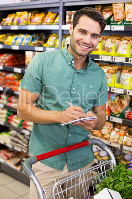 Portrait of smiling man writing on his notepad in aisle