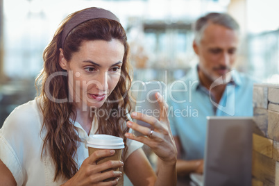 Pretty brunette using her smartphone with coffee in her hand