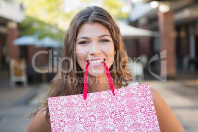 Portrait of smiling woman holding shopping bag in her mouth