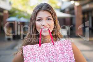Portrait of smiling woman holding shopping bag in her mouth