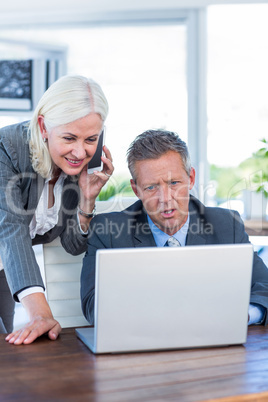 Businesswoman having phone call and looking at laptop with her c