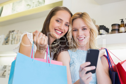 Happy women smiling at camera and holding smartphone