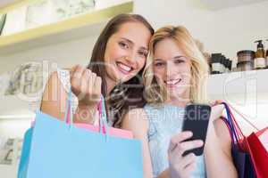 Happy women smiling at camera and holding smartphone
