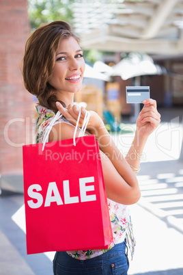 Portrait of smiling woman with sale shopping bag showing credit