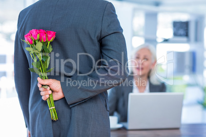 Businessman hiding flowers behind back for colleague