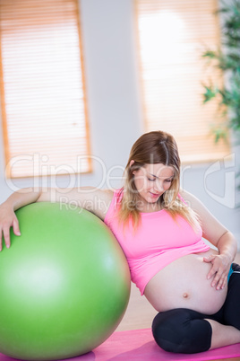 Pregnant woman touching her belly next to exercise ball