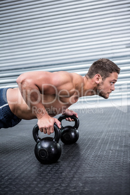 Muscular man doing push-ups with kettlebells