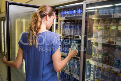 Pretty woman taking bottle of water in fridge