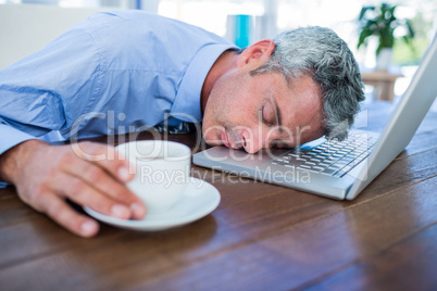 Businessman sleeping on laptop computer and touching coffee cup