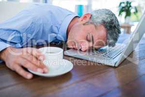 Businessman sleeping on laptop computer and touching coffee cup