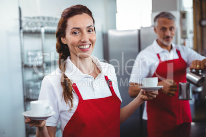 Pretty barista holding cups of coffee with colleague behind