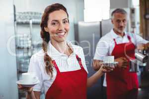 Pretty barista holding cups of coffee with colleague behind
