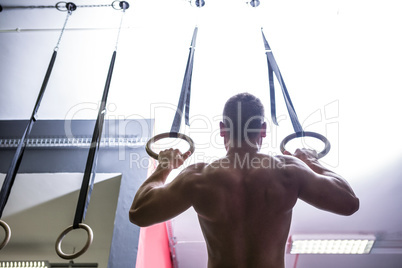 Back view of muscular man doing ring gymnastics