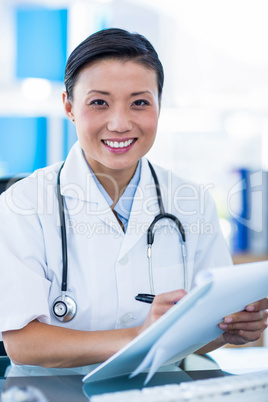 Happy doctor writing on a clipboard and smiling at camera