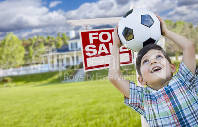 Boy Holding Ball In Front of House and Sale Sign