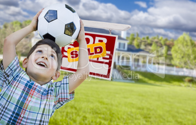 Boy Holding Ball In Front of House and Sold Sign