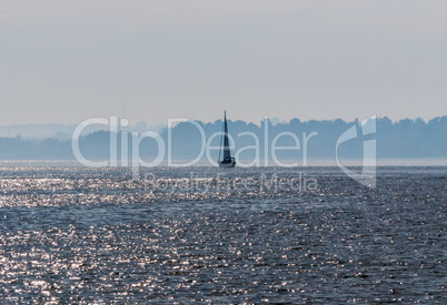 Sailboat on water against hazy shoreline