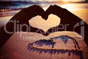 Composite image of hands making heart shape on the beach