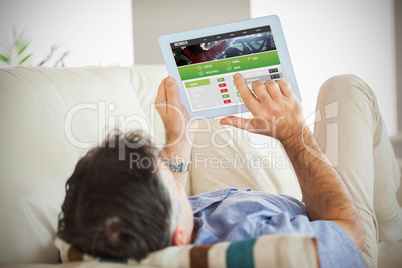 Composite image of man laying on sofa using a tablet pc