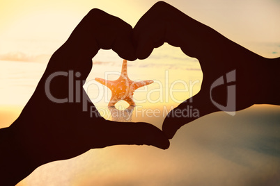 Composite image of couple making heart shape with hands