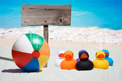 Sechs bunte Gummienten und ein Holzschild am Strand