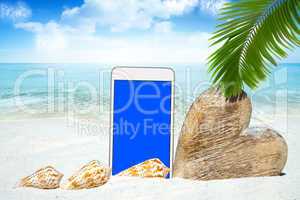 Smartphone, Herz aus Holz und Muscheln am Strand