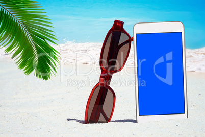 Weißes Smartphone, Sonnenbrille unter Palmwedel am Strand