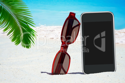 Schwarzes Smartphone, Sonnenbrille unter Palmwedel am Strand