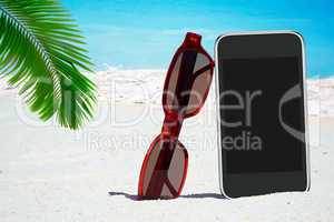 Schwarzes Smartphone, Sonnenbrille unter Palmwedel am Strand