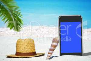 Weißes Smartphone und Strohhut unter Palmwedel am Strand