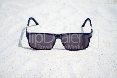Einzelne Sonnenbrille liegt am Sandstrand