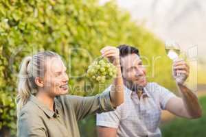 Two young happy vintners holding a glass of wine and grapes