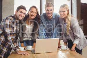 Smiling friends standing around laptop