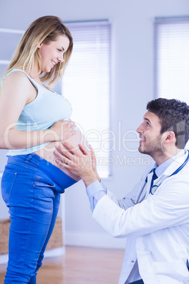 Smiling doctor checking stomach of standing pregnant patient