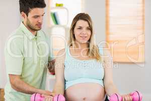 Pregnant woman sitting on exercise ball and lifting dumbbells