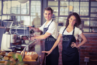 Smiling waitress in front of colleague making coffee