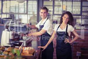 Smiling waitress in front of colleague making coffee