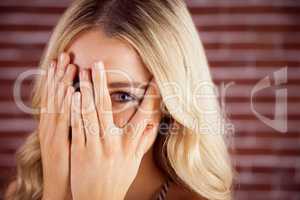 Beautiful blonde woman hiding behind hands