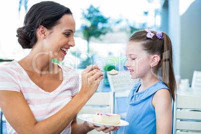 Mother feeding her daughter with cake