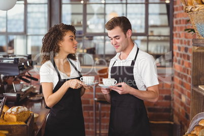 Smiling waiter and waitress holding cup of coffee