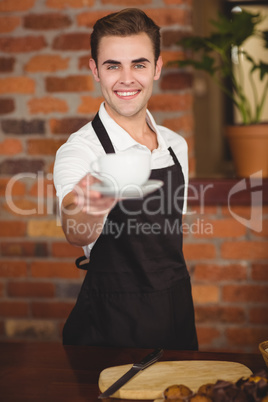 Smiling barista offering cup of coffee to camera