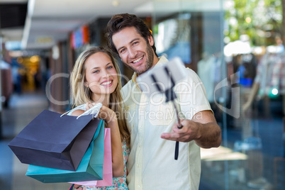 Smiling couple with shopping bags taking selfies with selfiestic
