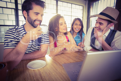 Laughing friends drinking coffee and looking at laptop