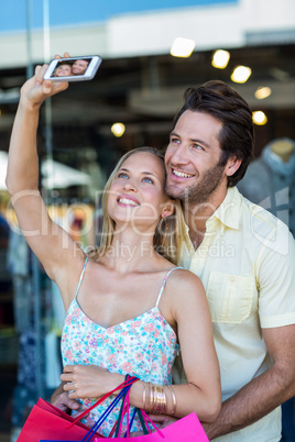 Smiling couple with shopping bags taking selfies