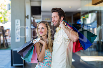 Smiling couple with shopping bags looking far away