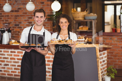 Smiling waiter and waitress holding tray with muffins